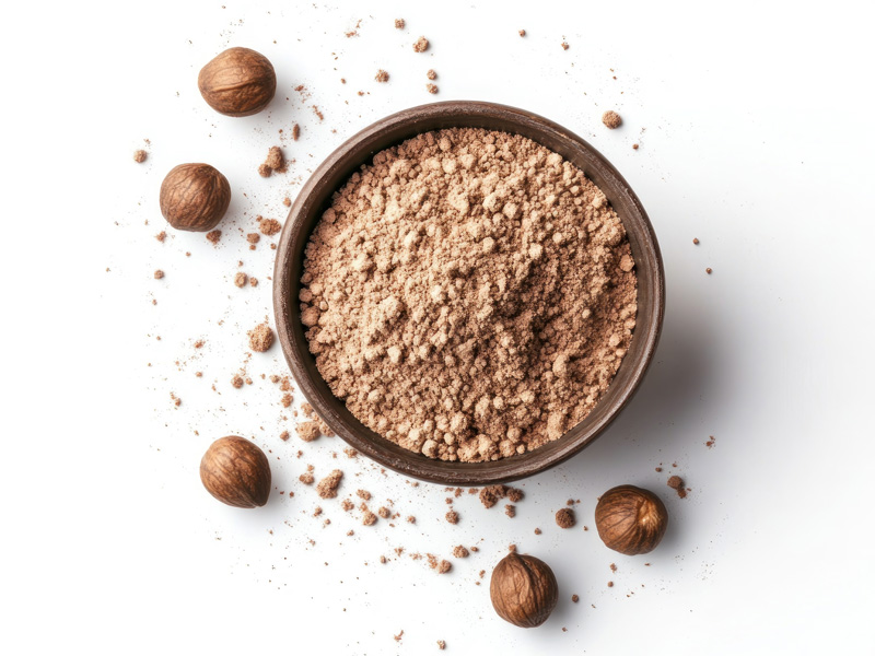 A bowl of hazelnut protein powder with scatted walnuts around the bowl